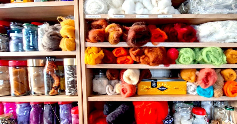 Workroom shelves of jars and tins holding dyed wool fibre, with a Jacob's biscuit tin
