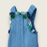 Close up of Blue merino baby dungarees showing green buttons and printed tartan trim.
