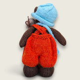 Back view of Bracken Moss Pebblewood collectible bear showing his hand-knitted rust dungarees, blue hat and satchel.