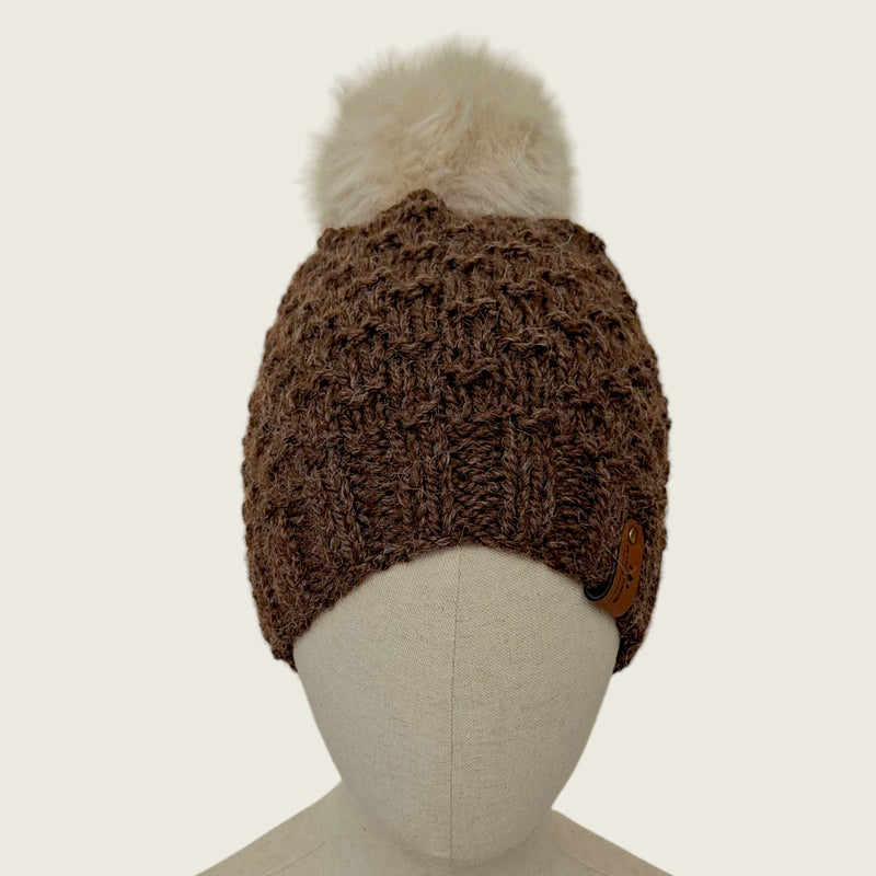 The dark brown hat on a mannequin, showing its full shape from brim to pompom