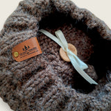 Close-up of the textured knit, leatherette tag, wooden button and pompom ribbon