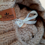 Close-up of the textured knit, leatherette tag and the ribbon that holds the pompom