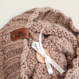Close-up of the textured knit, leatherette tag and wooden pompom button