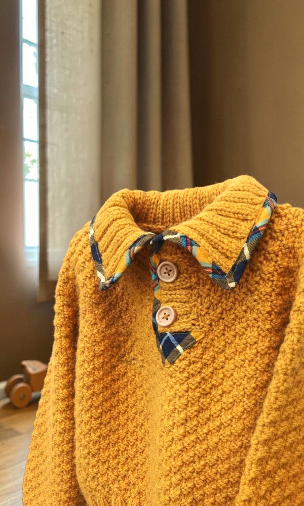 Mustard hand-knitted toddler jumper with checked collar and wooden buttons in a softly lit child’s room.