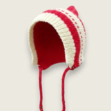 Side view of red and ivory handknitted merino wool baby bonnet with knitted ties.