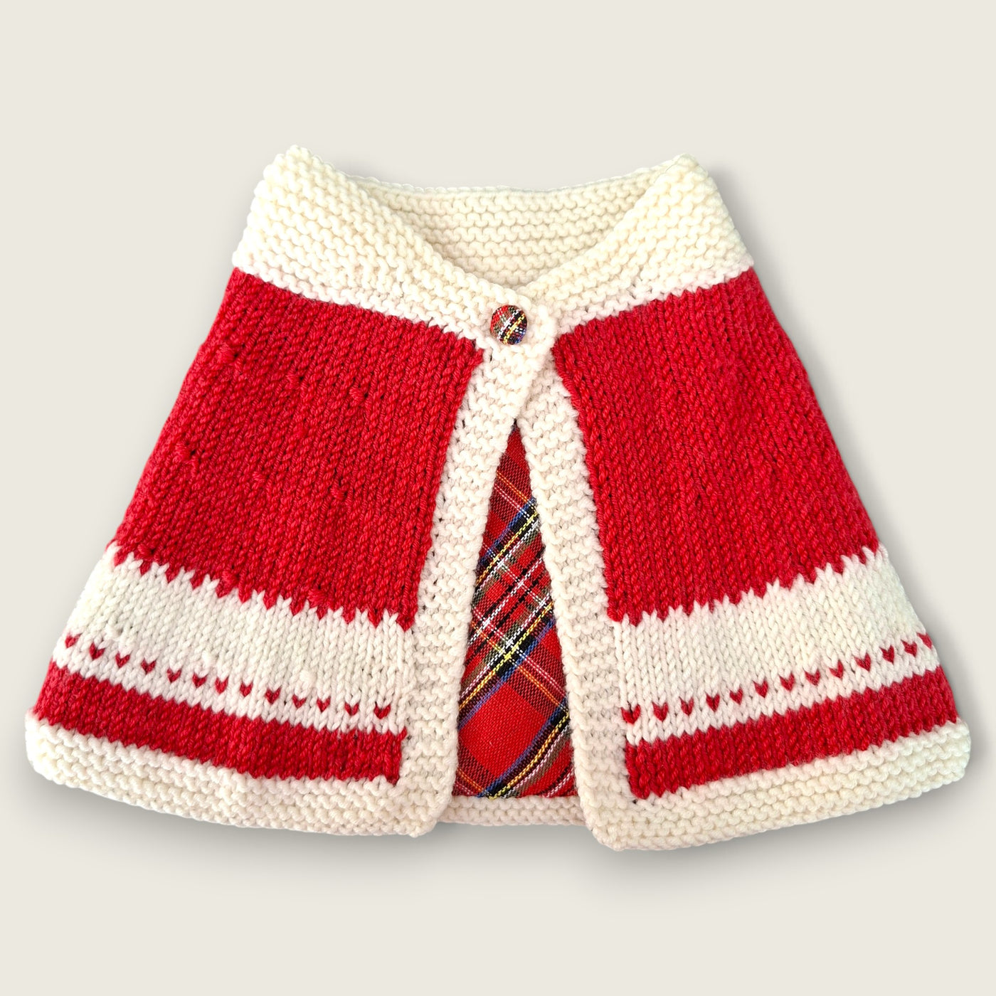 Red and ivory handknitted merino baby capelet with tartan detail and decorative button.