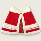 Red and ivory handknitted merino baby capelet with tartan detail and decorative button.