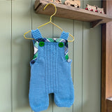 Blue merino baby dungarees hanging in a natural nursery setting.