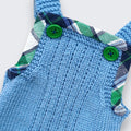 Close up of green wooden buttons and green and navy tartan trim on hand knitted merino baby dungarees - original design by The Crafty Pebblers Ireland
