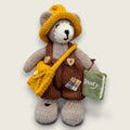 Hazel Hollow, Pebblewood collectible bear and Story Keeper, wearing brown dungarees with a knitted hat and satchel, carrying his needle-felted book of stories.