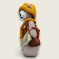 Left side view of Hazel Hollow, a hand-knitted Pebblewood collectible bear wearing brown dungarees, mustard knitted hat and satchel.