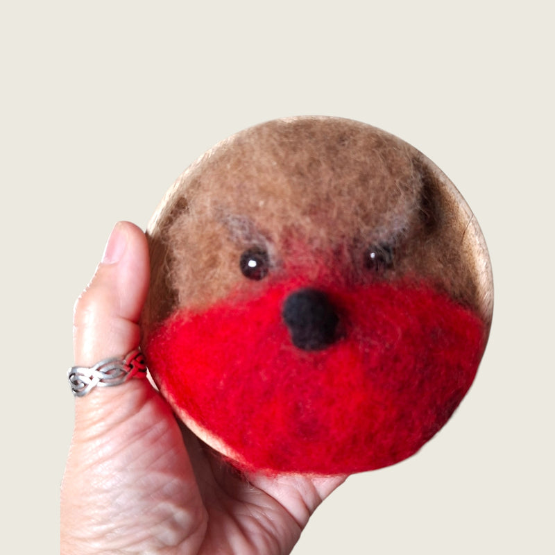 Hand needle-felted robin face mounted in a small wooden bowl, shown in hand to demonstrate its scale.