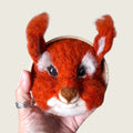 Hand needle-felted red squirrel face mounted in a small wooden bowl, shown in hand to demonstrate its scale.