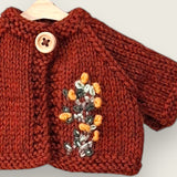 Close-up of dark rust wool cardigan with hand embroidered wildflowers and wooden button