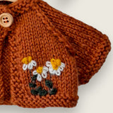 Close-up of rust wool cardigan with three hand embroidered daisies