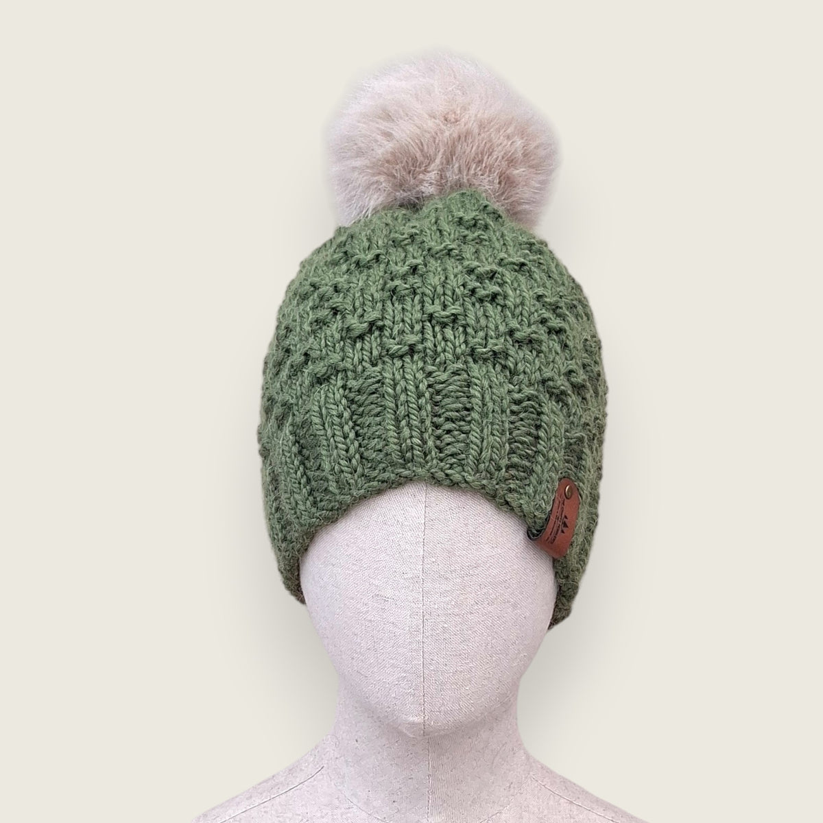 Sage green handknitted alpaca and wool hat with a mink-coloured faux fur pompom, front view