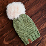 The sage green knitted hat lying flat on a dark wooden table