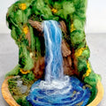Front view of The Living Fall, a handcrafted 3D felted wool sculpture featuring a waterfall, rock faces, wildflowers and moss in a wooden bowl.