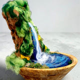 Side view of The Living Fall, a handcrafted 3D felted wool sculpture showing the waterfall flowing into a pool within a wooden bowl.