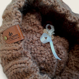 Close-up of the textured knit, leatherette tag and the ribbon that holds the pompom