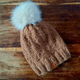 The toffee knitted hat lying flat on a dark wooden table