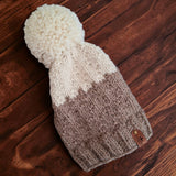 The two tone fawn and natural colour hand knitted hat lying flat on a dark wooden table