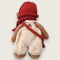 Back view of Willow Hearth showing the hand-knitted cream dungarees, rust-red hat, scarf and satchel strap.
