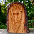 Hand-carved lime wood Woodland Face sculpture with natural live edge displayed in a woodland setting.