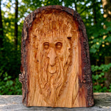 Hand-carved lime wood Woodland Face sculpture with natural live edge displayed in a woodland setting.